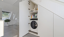Platz unter der Dachschräge für einen Schrank genutzt, der Platz für Waschmaschine, Trockner und Waschmittel bietet.