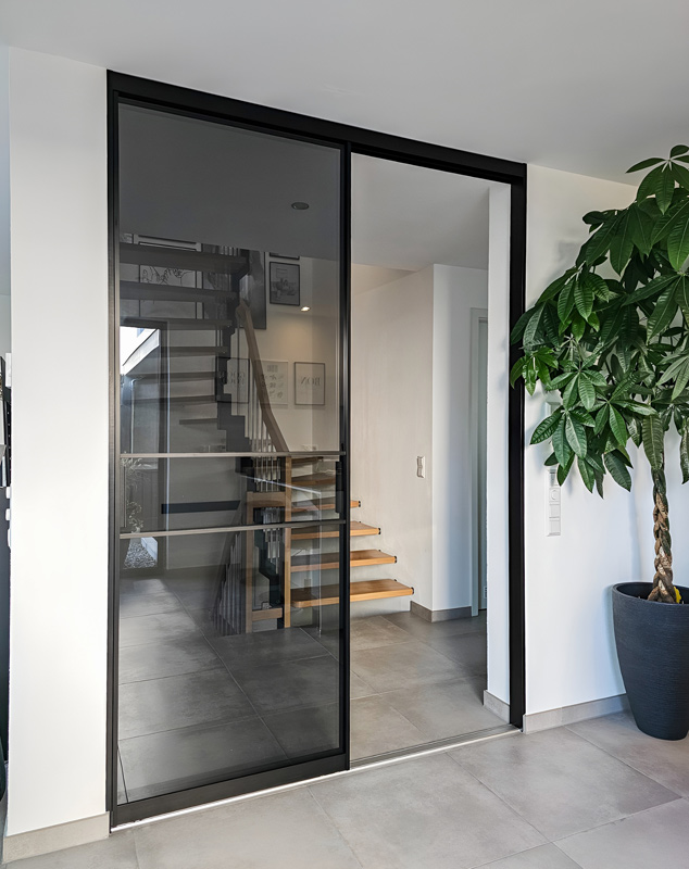 Moderne Glasraumteiler mit schwarzen Rahmen und dunklem Rauchglas im Eingangsbereich eines Hauses